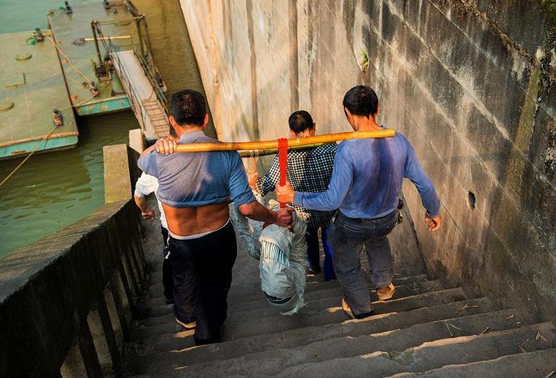 两人用扁担合力抬货走下江边石阶